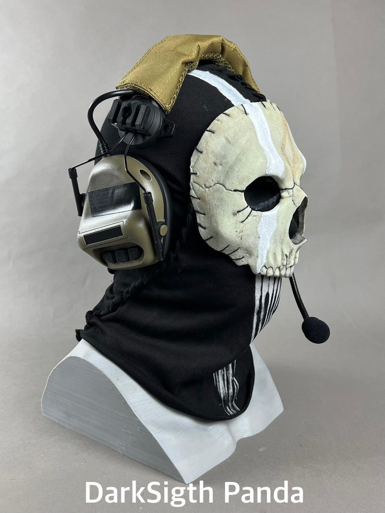 May include: A black and tan Ghost mask with a skull design, white vertical stripe, and attached headset. The mask is on a white stand. The text "DarkSigth Panda" is at the bottom.