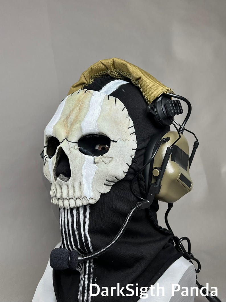May include: A black balaclava with a skull mask, white stripes, and a tan headset. The skull mask has a stitched design with white and tan accents. The headset has a microphone attached. The text "DarkSigth Panda" is visible.