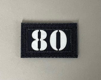May include: Black rectangular patch with the number "80" in white block letters. The patch has a black border and the text "A.R.K SMITH" at the bottom.