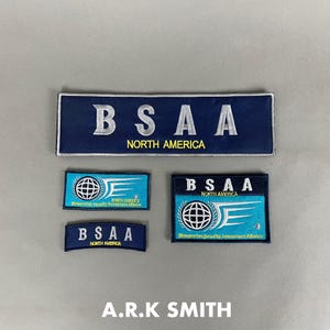 Può includere: Una collezione di toppe ricamate di varie forme e dimensioni. Le toppe sono principalmente blu navy e turchese, con le lettere "BSAA" e le parole "NORTH AMERICA". Alcune toppe includono un globo e ali stilizzate. Il testo "A.R.K SMITH" è in basso.