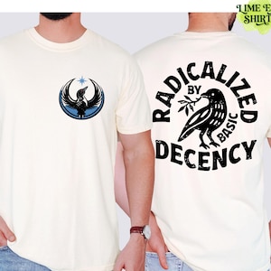 May include: Cream-coloured t-shirt with a black and blue bird emblem on the front. The back of the shirt features a black raven graphic and the text "RADICALIZED BY BASIC DECENCY" in a circular design. The t-shirt has short sleeves.