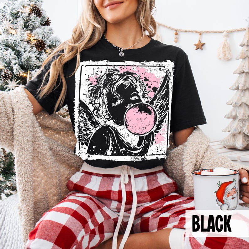 May include: Black t-shirt featuring a graphic of an angel blowing a bubblegum bubble. The angel is black and white, with pink accents. The word "BLACK" is printed in white on a black background.