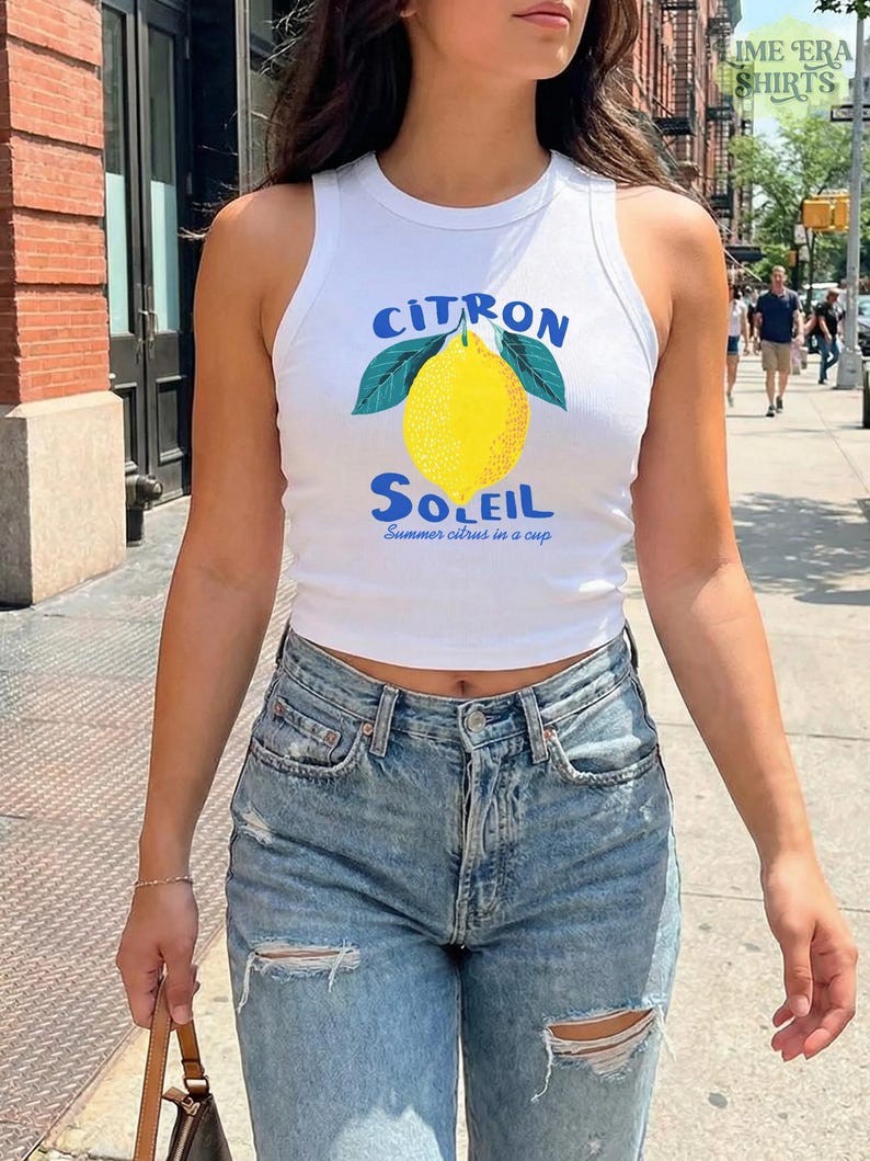Puede incluir: Una camiseta de tirantes blanca acanalada con un gr&aacute;fico de un lim&oacute;n amarillo con hojas verdes. El texto sobre el lim&oacute;n dice CITRON en azul, y el texto debajo dice SOLEIL en azul, seguido del texto m&aacute;s peque&ntilde;o Summer citrus in a cup.