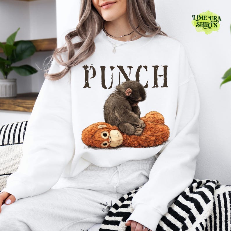 May include: White sweatshirt with the word "PUNCH" in brown letters. The graphic shows a brown monkey sitting on a brown stuffed animal. The sweatshirt is part of the Lime Era Shirts collection.