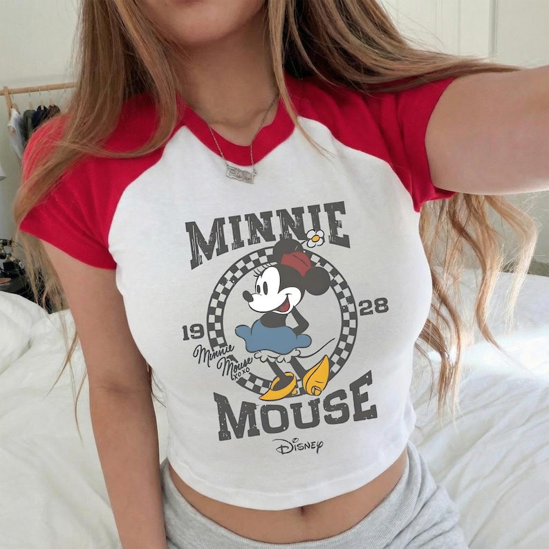 May include: White crop top with red sleeves featuring a Minnie Mouse graphic. The graphic includes the text "MINNIE MOUSE" and the Disney logo. The shirt has a classic baseball tee design.