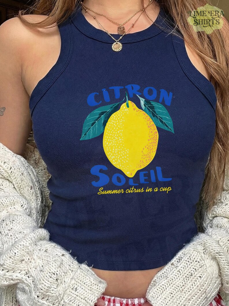 Puede incluir: Una camiseta de tirantes acanalada de color azul marino con un gr&aacute;fico de un lim&oacute;n amarillo con hojas verdes. El texto CITRON SOLEIL aparece en letras azules sobre y bajo el lim&oacute;n, con la frase amarilla Summer citrus in a cup debajo.