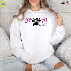 May include: White hoodie with the text "PhinisheD" in a script font, with a graduation cap graphic and the name "Dr. Jonas" below. The hoodie is a casual style, suitable for everyday wear.
