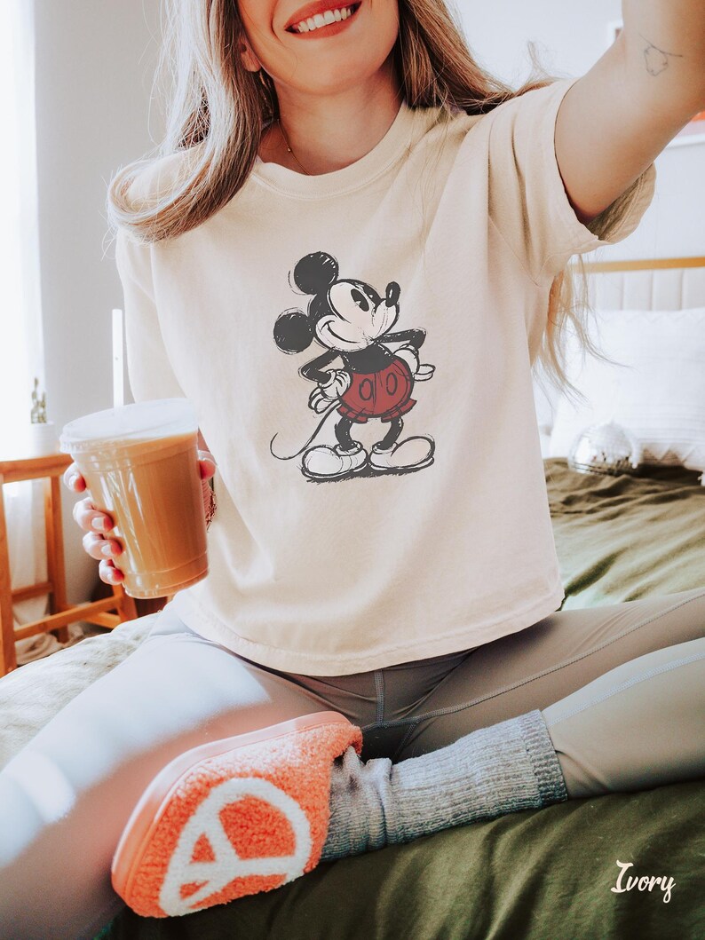 以下が含まれることがあります： アイボリー色のTシャツ。ミッキーマウスのイラストが黒、赤、白で描かれています。Tシャツはゆったりとしたフィット感で、半袖です。「Ivory」の文字が右下にプリントされています。