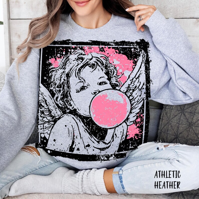 May include: Athletic heather gray sweatshirt featuring a graphic of a cherub blowing a pink bubblegum bubble. The cherub is in black and white with pink accents. The sweatshirt has long sleeves and a crew neck.