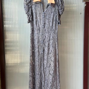 May include: A white ceramic mug with a black handle and the text "But First, Coffee" in a bold, black font. The mug is set against a blurred background, suggesting a cozy setting.