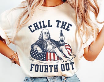 May include: An ivory short-sleeve t-shirt featuring a graphic of Benjamin Franklin holding a bottle while sitting in a red, white, and blue American flag-patterned pool float. The text CHILL THE FOURTH OUT is printed in dark blue block letters.