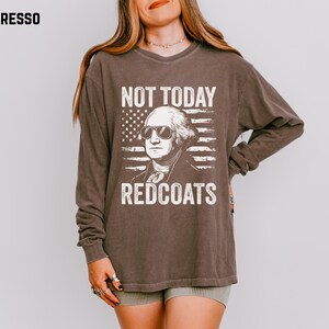 May include: Espresso-coloured long-sleeve shirt featuring a graphic of George Washington wearing sunglasses in front of an American flag. The text reads "NOT TODAY REDCOATS". The shirt has a vintage, worn appearance.
