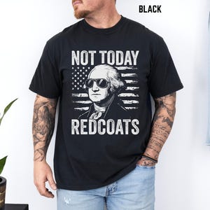 May include: Black crew neck t-shirt with a graphic of George Washington in sunglasses and an American flag. White text reads "NOT TODAY REDCOATS". The shirt is a standard fit.