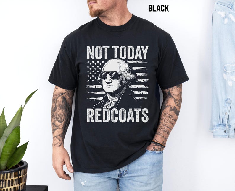 May include: Black crew neck t-shirt with a graphic of George Washington in sunglasses and an American flag. White text reads "NOT TODAY REDCOATS". The shirt is a standard fit.