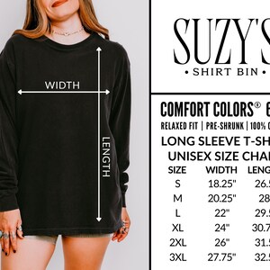 May include: Black long-sleeve t-shirt with a crew neck. The shirt has a unisex size chart with measurements in inches. The brand name "Suzy's Shirt Bin" is displayed. The shirt is made of 100% cotton and is pre-shrunk.
