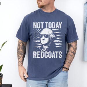 May include: A navy blue t-shirt featuring a graphic of George Washington wearing sunglasses against an American flag. The text "NOT TODAY REDCOATS" is printed in white. The word "DENIM" is in the top left corner.