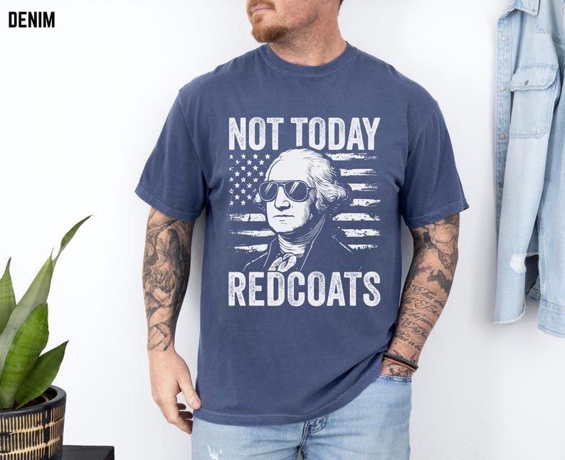 May include: A navy blue t-shirt featuring a graphic of George Washington wearing sunglasses against an American flag. The text "NOT TODAY REDCOATS" is printed in white. The word "DENIM" is in the top left corner.