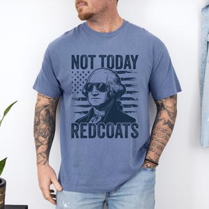 May include: Blue jean t-shirt featuring a graphic of George Washington in sunglasses, an American flag, and the text "NOT TODAY REDCOATS". The shirt is a solid blue colour.