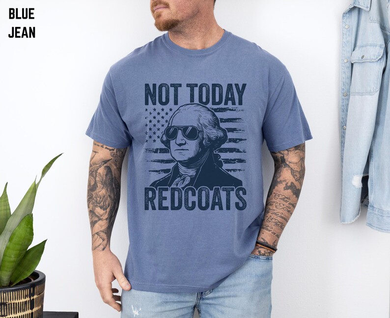 May include: Blue jean t-shirt featuring a graphic of George Washington in sunglasses, an American flag, and the text "NOT TODAY REDCOATS". The shirt is a solid blue colour.