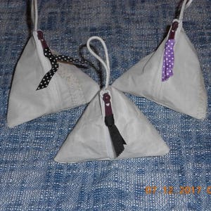 May include: Three triangular fabric pouches with zipper closures and ribbon ties. The pouches are white with black and white polka dot ribbon ties, white with purple and white polka dot ribbon ties, and white with black and white polka dot ribbon ties.