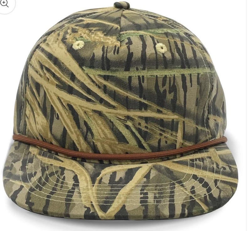 May include: A brown and green camouflage baseball cap with a brown leather band around the crown. The cap has a curved brim.