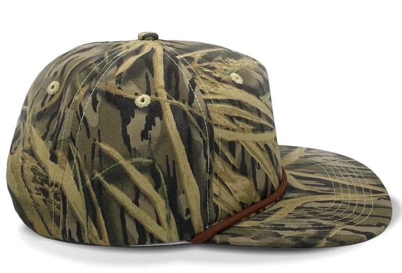 May include: A camouflage baseball cap with a brown leather strap. The cap is made of a soft, durable fabric and features a classic five-panel design.