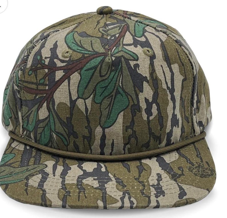 May include: A camouflage baseball cap with a green, brown, and black pattern. The cap has a brown brim and a green strap.