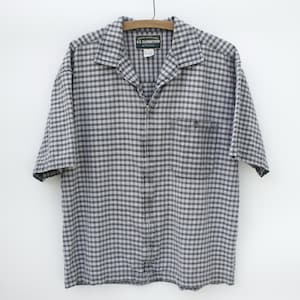 May include: A short-sleeved, zip-up plaid shirt with a chest pocket. The shirt is gray and white with a black plaid pattern. The label reads "U.S. Expedition" and "Adventure"