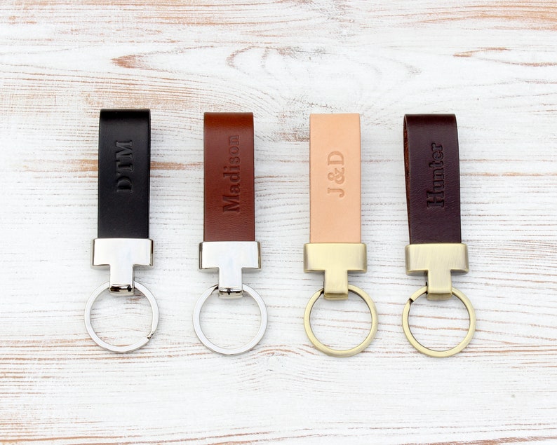 May include: Four leather keychains in black, medium brown, light tan, and dark brown. Each features a metal attachment and a circular ring. The leather straps are embossed with the names or initials DTM, Madison, J&D, and Hunter respectively.