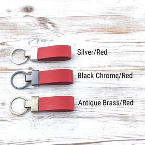 May include: Three red leather keychains with metal hardware. The top keychain has a silver ring, the middle has a black chrome ring, and the bottom has an antique brass ring. Text labels read Silver/Red, Black Chrome/Red, and Antique Brass/Red.