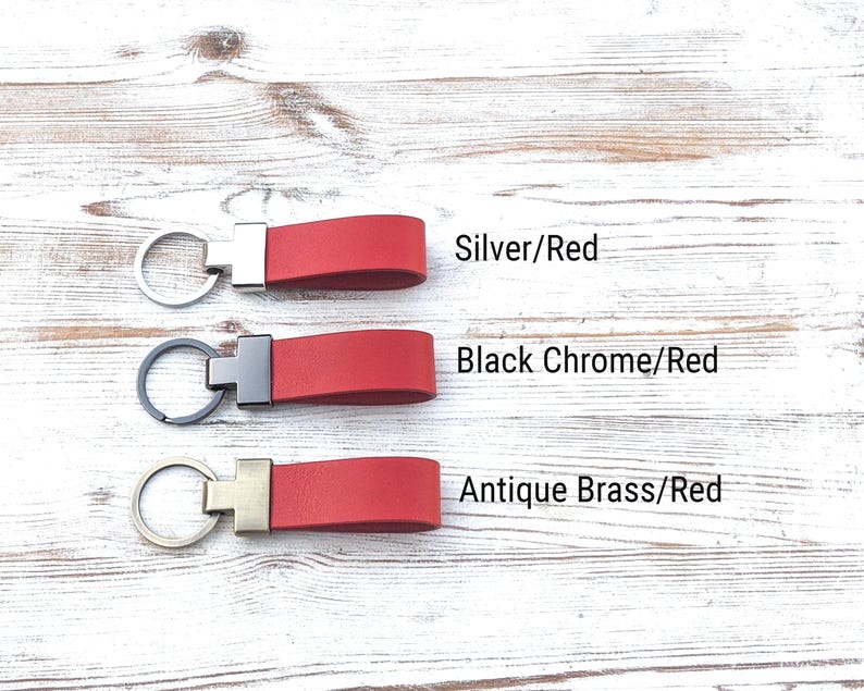 May include: Three red leather keychains with metal hardware. The top keychain has a silver ring, the middle has a black chrome ring, and the bottom has an antique brass ring. Text labels read Silver/Red, Black Chrome/Red, and Antique Brass/Red.