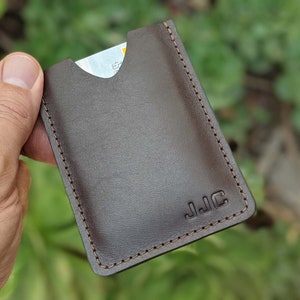 Personalized leather minimalist wallet with de-bossed initials being held in hand in front of greenery.