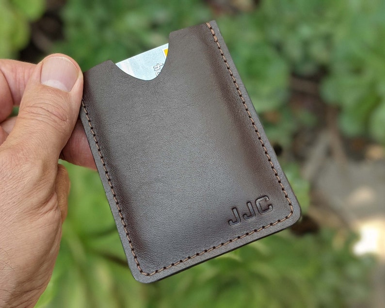 Personalized leather minimalist wallet with de-bossed initials being held in hand in front of greenery.