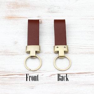 May include: Two brown leather keychains with brass-toned metal hardware and circular rings. One keychain is labelled Front, showing a smooth surface, and the other is labelled Back, showing two small metal screws securing the leather strap to the hardware.