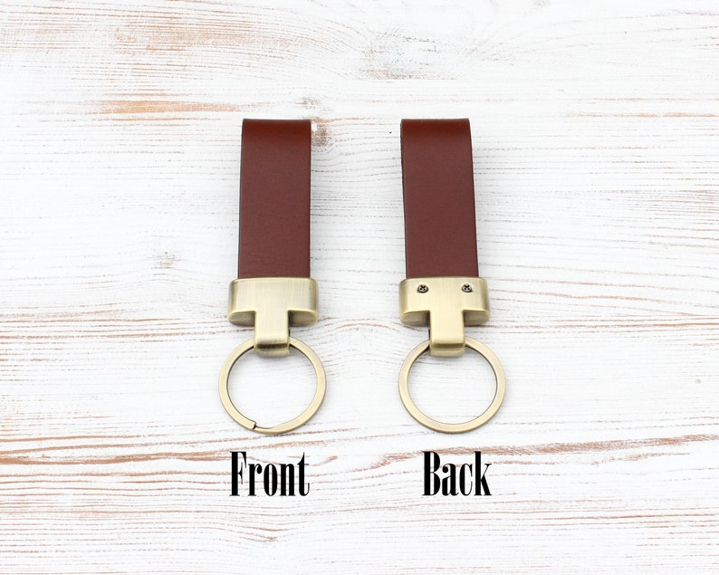 May include: Two brown leather keychains with brass-toned metal hardware and circular rings. One keychain is labelled Front, showing a smooth surface, and the other is labelled Back, showing two small metal screws securing the leather strap to the hardware.