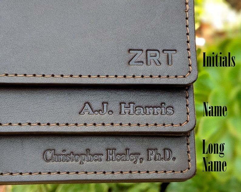 Three dark brown leather business card holders are stacked, each with different customization. One card case is personalized with initials, one with a name, and one with a long name.