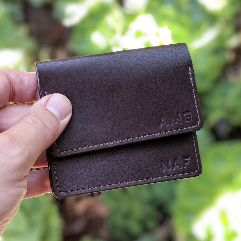 Two leather business card holders with personalized initials being held.