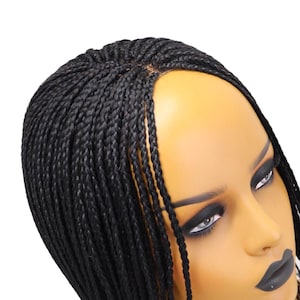 May include: A black braided wig displayed on a mannequin head. The wig is made up of small, tightly woven braids. The mannequin has dark makeup and a neutral skin tone, set against a white background.
