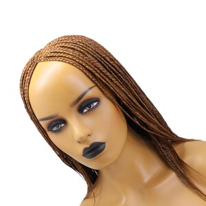 May include: A mannequin head with a brown braided wig. The mannequin has dark eye makeup and black lipstick. The wig is styled with small, individual braids that cascade down the sides.
