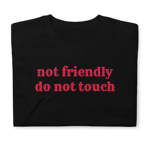 May include: Black t-shirt featuring the red text "not friendly do not touch". The text has a decorative font with a blue outline. The shirt is folded and appears to be made of a soft material.
