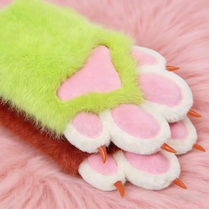 May include: Close-up of furry paw gloves in shades of green, brown, and white. The paw pads are pink, with orange claws. The gloves are on a pink, fluffy surface.