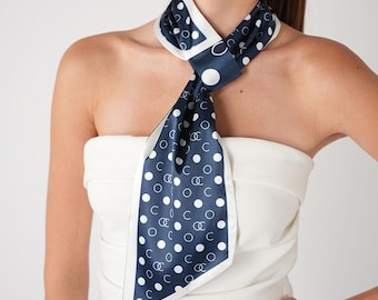 May include: A navy blue and white polka dot scarf with a white border. The scarf is tied around the neck. The scarf has a repeating pattern of white circles and the letter "C".