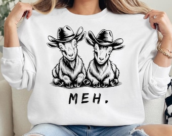 May include: White sweatshirt with a black and white illustration of two goats wearing cowboy hats. The goats are sitting down and looking at the viewer. The text "MEH." is printed below the goats.