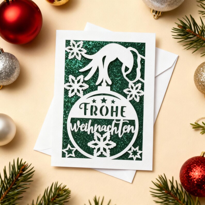 Peut inclure: Une carte de No&euml;l blanche avec un fond vert paillet&eacute; et un motif d'ornement d&eacute;coup&eacute;. L'ornement porte le texte allemand "Frohe Weihnachten" et est entour&eacute; de flocons de neige et d'&eacute;toiles. La carte est pos&eacute;e sur une surface beige clair avec des d&eacute;corations de No&euml;l et des branches de pin.