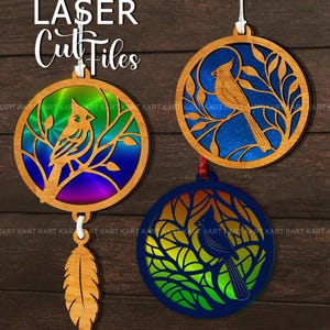 May include: Laser-cut wooden ornaments featuring bird designs within circular frames. The ornaments showcase birds perched on branches, with colorful backgrounds of blue, green, and purple. One ornament has a feather pendant.