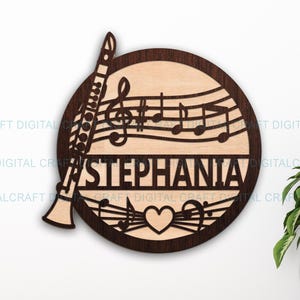 Può includere: Arte da parete musicale in legno con un clarinetto, note musicali e il nome "STEPHANIA". Il design include un simbolo a forma di cuore ed è realizzato in legno marrone chiaro e scuro, per gli amanti della musica.