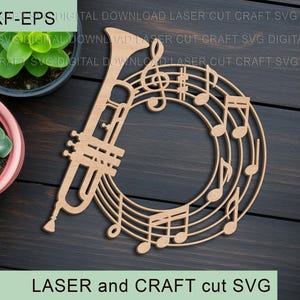 Puede incluir: Un diseño de madera cortado con láser que presenta una trompeta y notas musicales dispuestas en un patrón circular. El diseño incluye el texto "LASER and CRAFT cut SVG". La imagen está sobre un fondo de madera oscura.