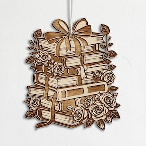 May include: Wooden ornament featuring a stack of books tied with a ribbon and adorned with roses and leaves. The ornament is made of light brown wood and is designed with intricate details, perfect for book lovers.