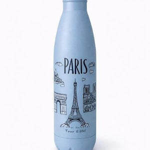 Peut inclure: Une gourde isotherme bleu clair avec un bouchon argenté. La gourde présente un dessin au trait noir de monuments parisiens, dont la Tour Eiffel, l'Arc de Triomphe et Notre-Dame, avec le mot "PARIS" au-dessus.