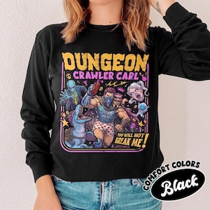 May include: A black long-sleeve shirt featuring a graphic print with the text "DUNGEON CRAWLER CARL" and "YOU WILL NOT BREAK ME!". The illustration depicts a central muscular figure in heart-patterned boxers surrounded by various fantasy characters.